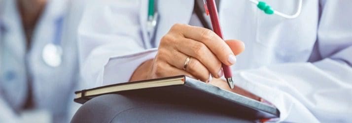 A doctor is jotting down notes in a notebook while answering frequently asked questions.