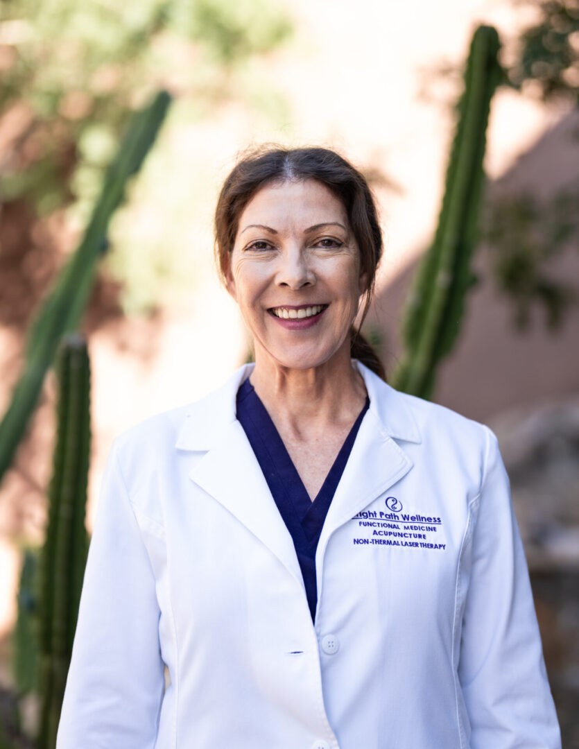 A woman in white lab coat standing next to cactus.